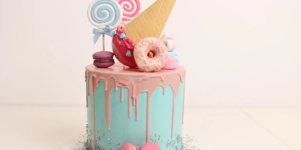 Bunter Drip Cake mit rosa Glasur, Lollis, Macarons und einem Eiswaffel-Horn.