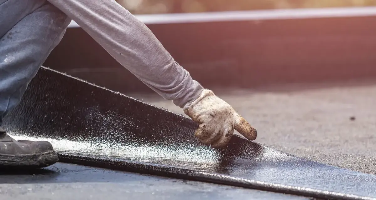Hand mit Handschuh legt neue Dachpappe an. Alte Dachpappe entsorgen ist der nächste Schritt.