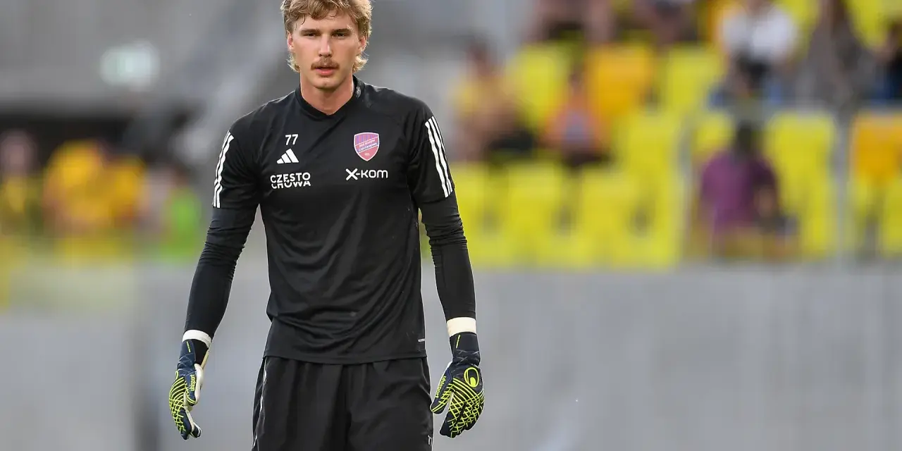 Mateusz Zych, bramkarz w czarnej koszulce z numerem 77, gotowy do akcji na boisku.