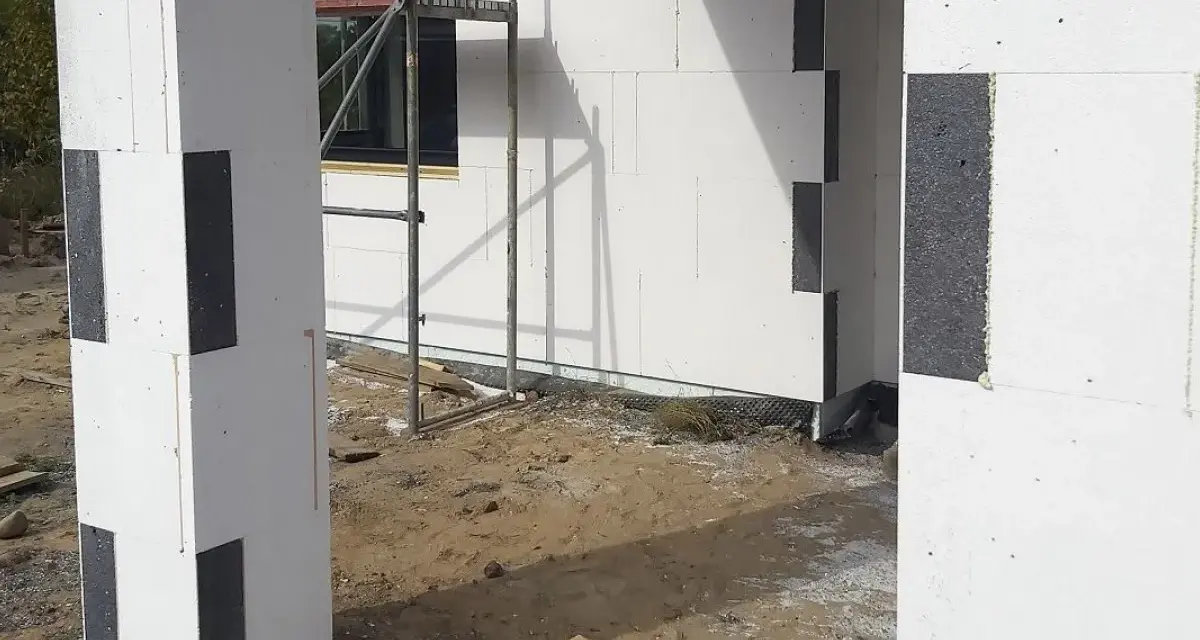 Budowa domu z bloczków styropianowych. Czy trzeba kołkować styropian grafitowy? Widok na fragment ściany i słupa z szarego styropianu.