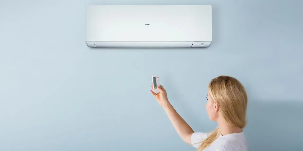 Donna con telecomando regola il condizionatore Haier. Il suo significato è il comfort climatico.