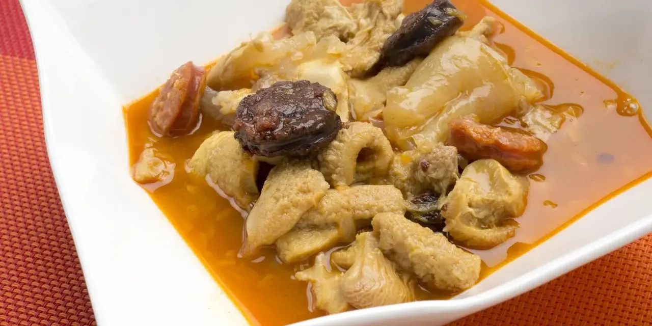 Un plato de callos a la madrileña con chorizo y morcilla en una cazuela blanca.