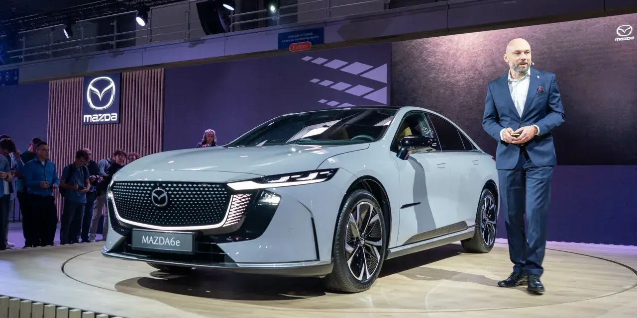 Elegancki, szary sedan Mazda6e prezentowany na scenie przez mężczyznę w garniturze.