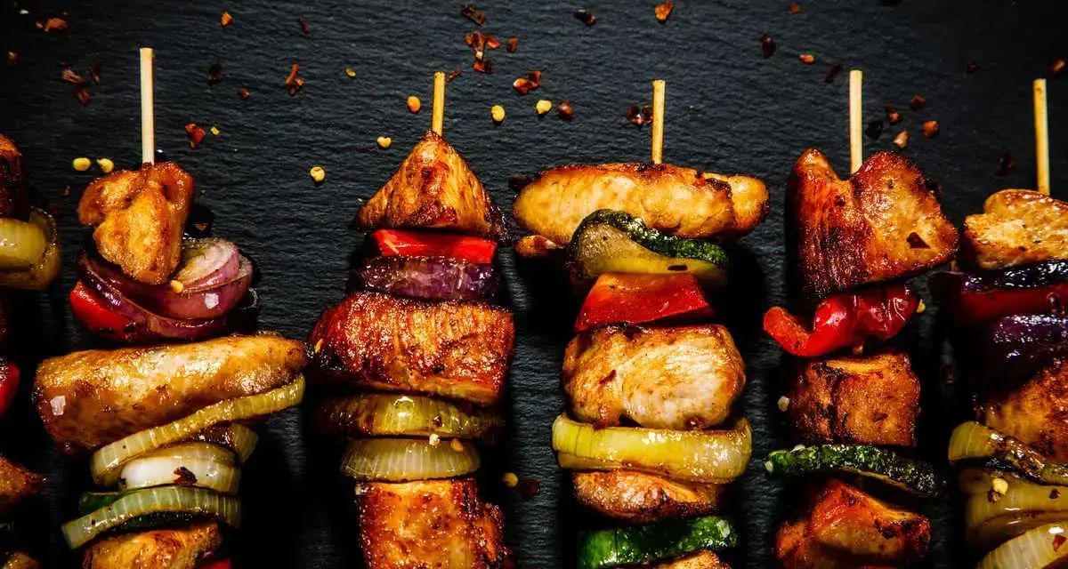 Spiedini di carne succulenti e colorati, alternati a cipolle, peperoni e zucchine, pronti per essere gustati.