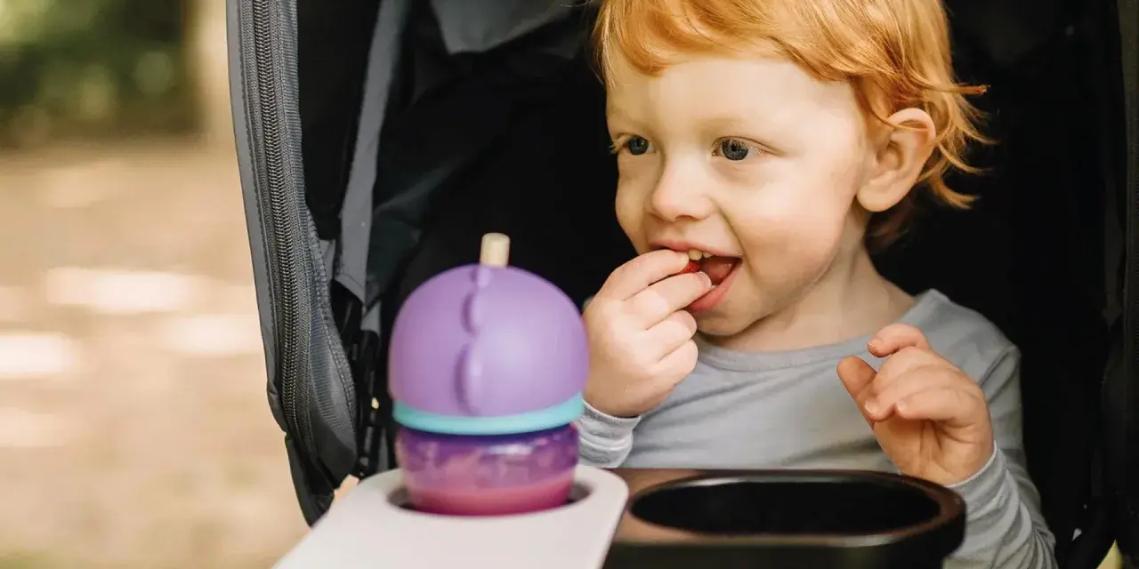 Rotschopf-Kind im Kinderwagen, isst genüsslich einen Snack. Dieses Kind hat immer Hunger und freut sich über jede Leckerei.