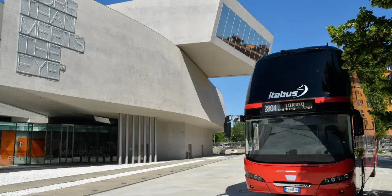 Autobus Itabus rosso e nero davanti a un edificio moderno con la scritta "More Than Meets The Eye". Un viaggio da Verona a Jesolo?