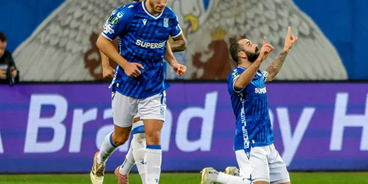 Piłkarz klęczy na boisku, celebrując bramkę. W tle biegnie kolega z drużyny. Wszyscy w niebieskich strojach. Czekamy, kiedy wraca ekstraklasa!