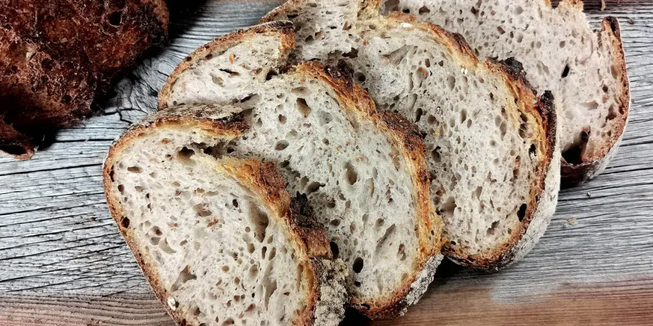 Ein Laib Sauerteigbrot, angeschnitten, mit sichtbarer, knuspriger Kruste. Die Scheiben zeigen eine luftige Krume. Hoffentlich ist die brotkruste zu hart, um sie zu genießen.