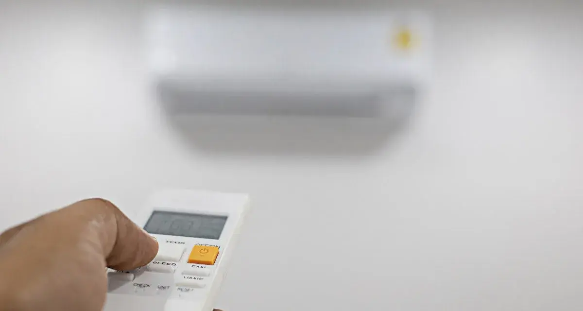 Mano che preme il telecomando per regolare il condizionatore. Il suo significato è comfort e controllo della temperatura.