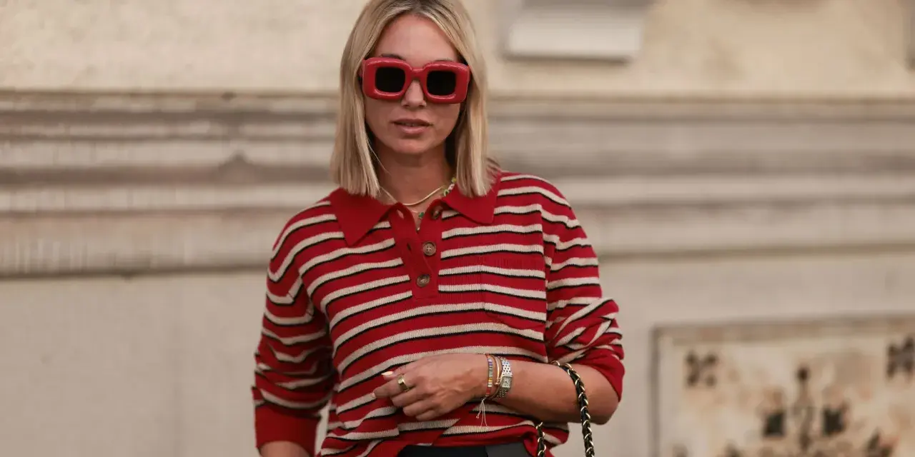 Donna con occhiali rossi oversize e maglione a righe rosse e bianche, un look che evoca un sofisticato preppy style.