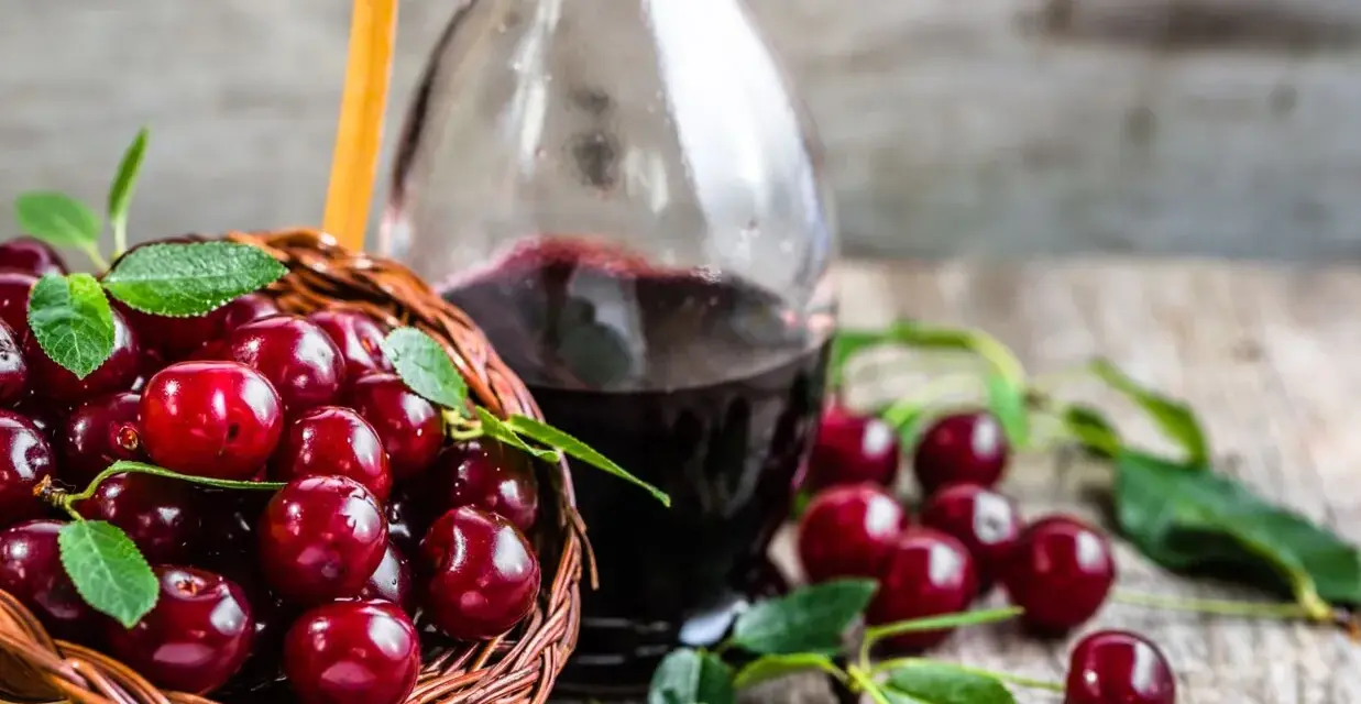 Koszyk pełen wiśni i butelka nalewki z wiśni – przepis babci. Aromatyczny trunek gotowy do degustacji.