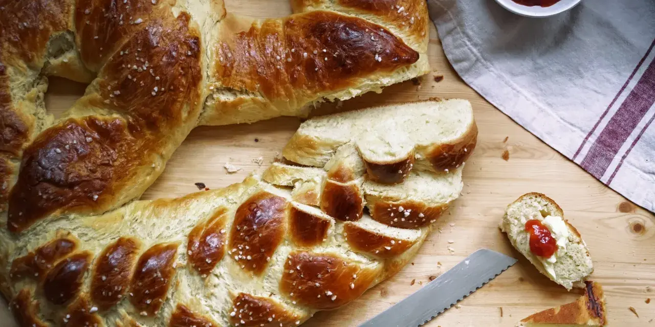 Goldbraune Neujahrsbrezel, mit Salz bestreut, auf einem Holztisch. Ein Stück ist mit Butter und Marmelade belegt. Ein tolles Neujahrsbrezel Rezept!