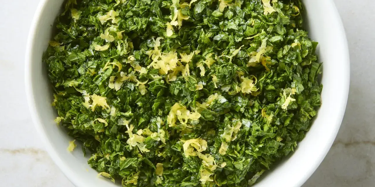 Un cuenco blanco lleno de perejil picado y ralladura de limón, perfecto para un toque fresco en tu cocina, como la albahaca en francés.