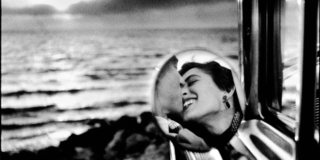 Un doux reflet dans le rétroviseur d'une voiture, une femme rit aux éclats, le regard tourné vers la mer.
