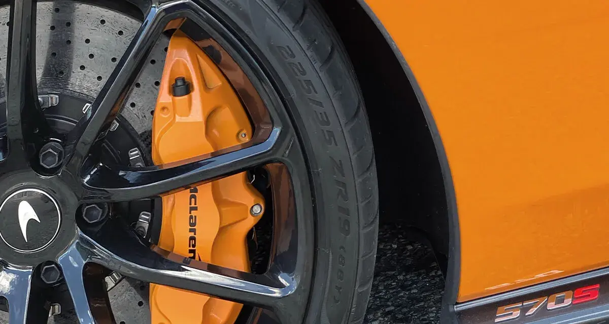 Pomarańczowy zacisk hamulcowy McLaren na czarnym, wieloramiennym kole. Opona z napisem 225/35 ZR19.