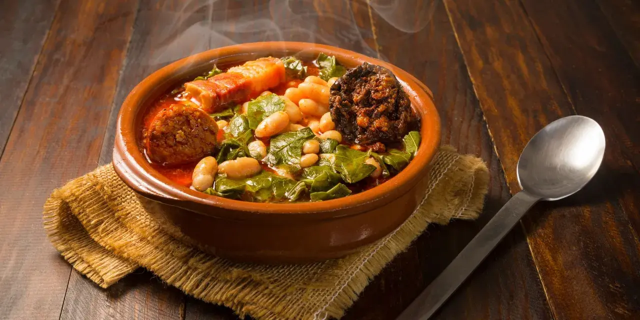 Un humeante pote asturiano, con fabes, berzas, chorizo y tocino, servido en cazuela de barro sobre arpillera.