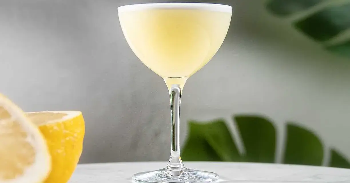 En elegant lemon martini med en lätt skumkrona, serverad med färska citronklyftor i bakgrunden.