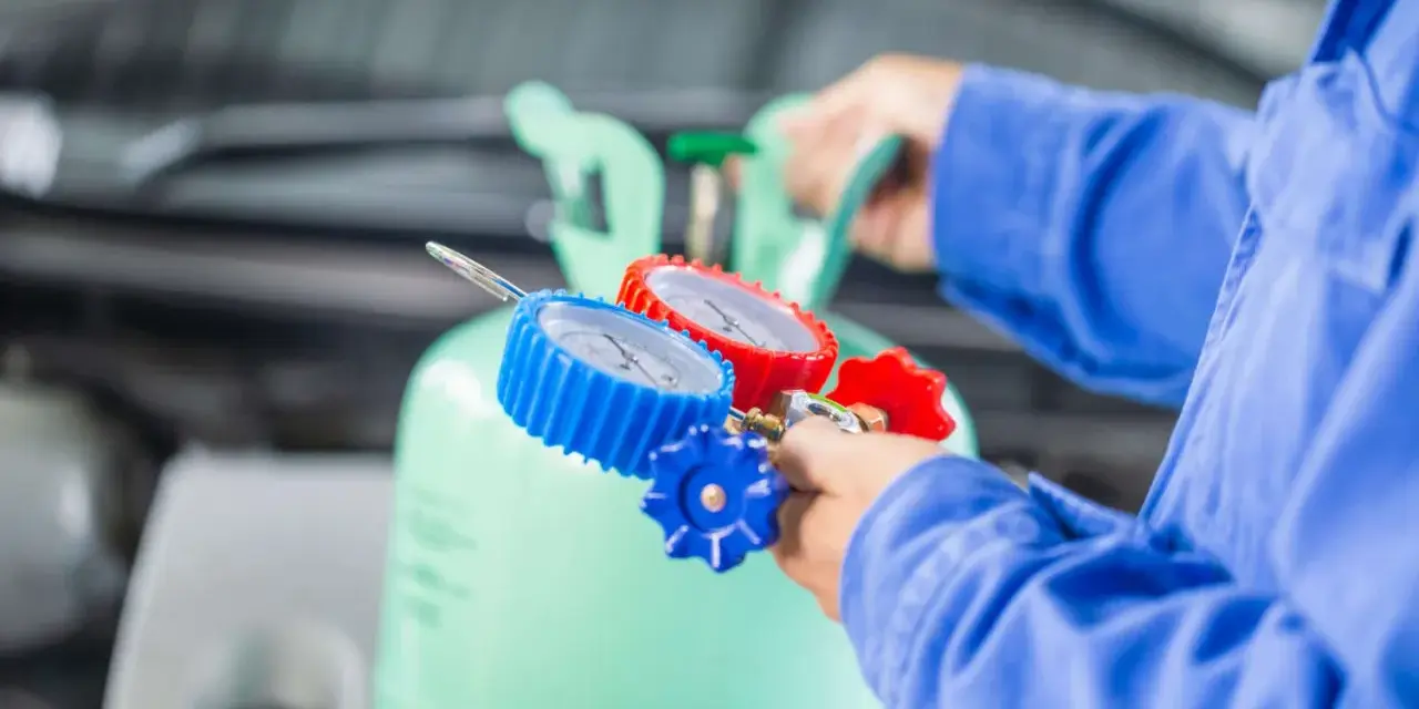 Mechanik podłącza manometry do butli z czynnikiem R32, przygotowując się do serwisu klimatyzacji samochodowej.