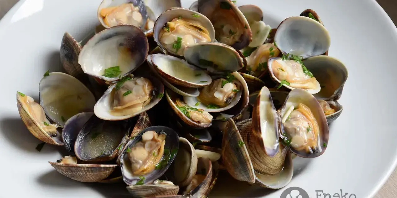Un plato de almejas a la marinera, jugosas y recién cocinadas, con perejil picado.