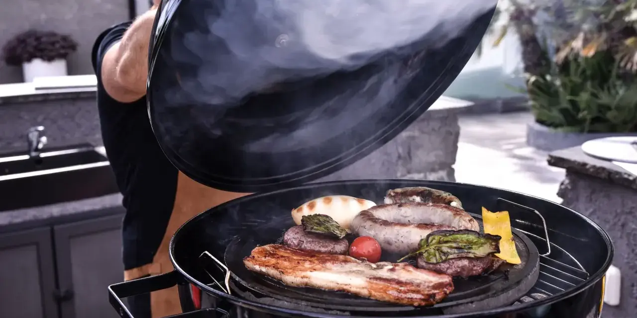 Fumo sale da una grigliata di carne succulenta, con salsicce, hamburger e pancetta che sfrigolano.