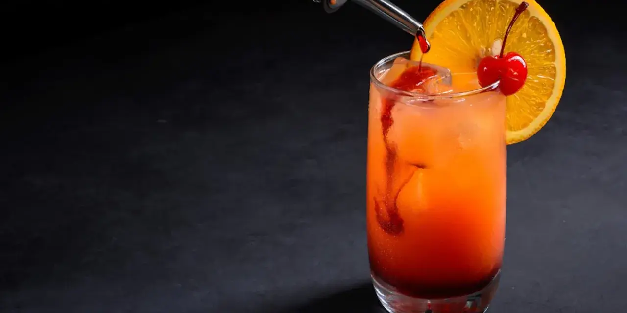 Kolorowy drink z syropem grenadina, ozdobiony plasterkiem pomarańczy i wisienką.