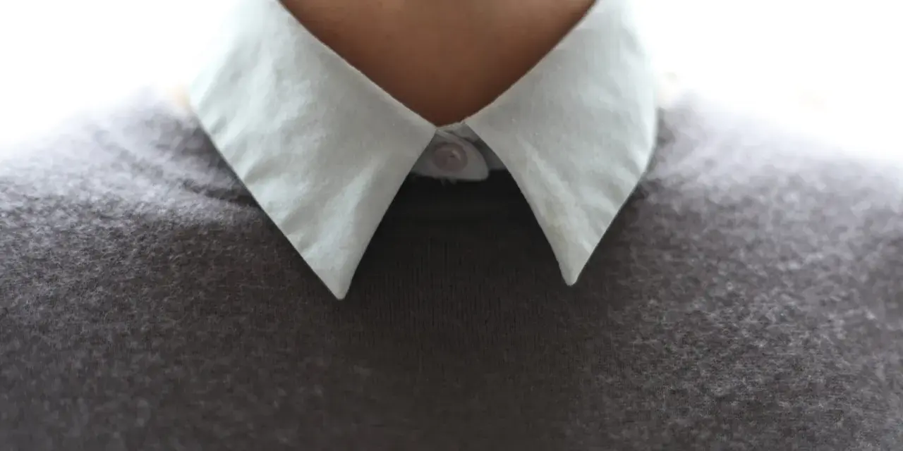 Gros plan sur un col froncé blanc sur un pull gris.