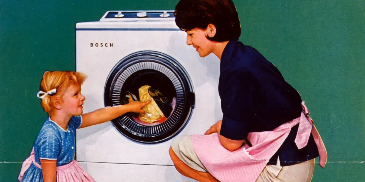 Mutter und Kind vor der ersten Waschmaschine. Das kleine Mädchen hilft beim Einräumen der Wäsche.