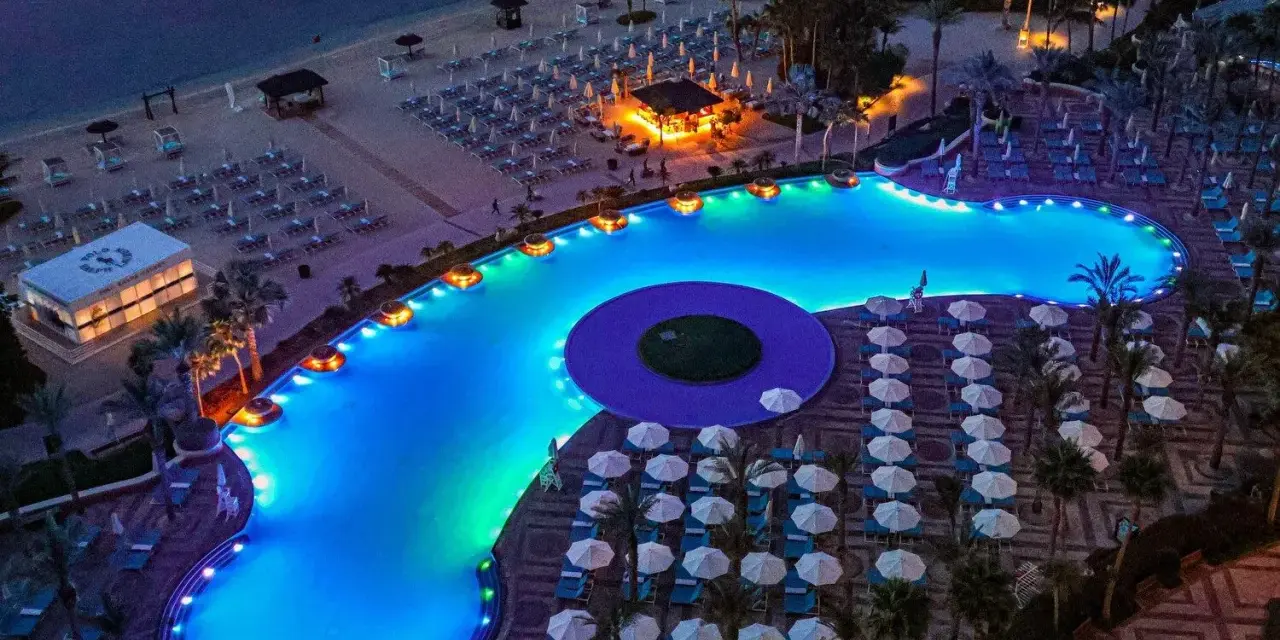Luksusowy basen z niebieskim podświetleniem i leżakami na plaży w Dubaju.