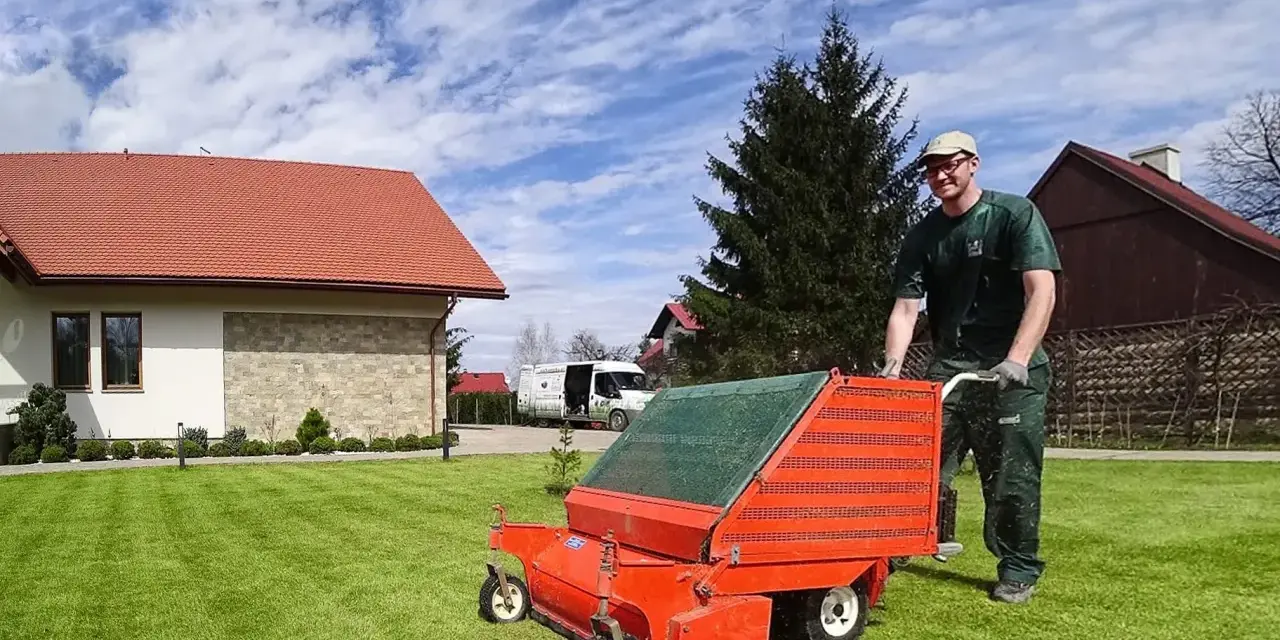 Mężczyzna z wertykulatorem na trawniku. Wertykulacja latem to klucz do zdrowej, zielonej murawy.