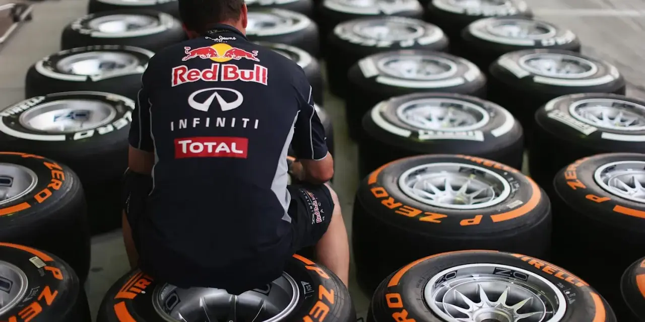 Mechanik w stroju Red Bulla siedzi wśród rzędów opon F1.