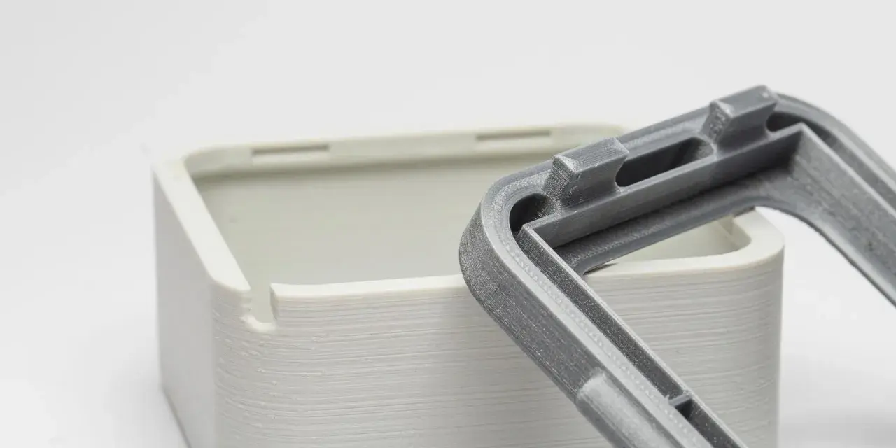 Close-up of a 3D-printed white box and a grey lid, showcasing the intricate snap fit joints designed for easy assembly.