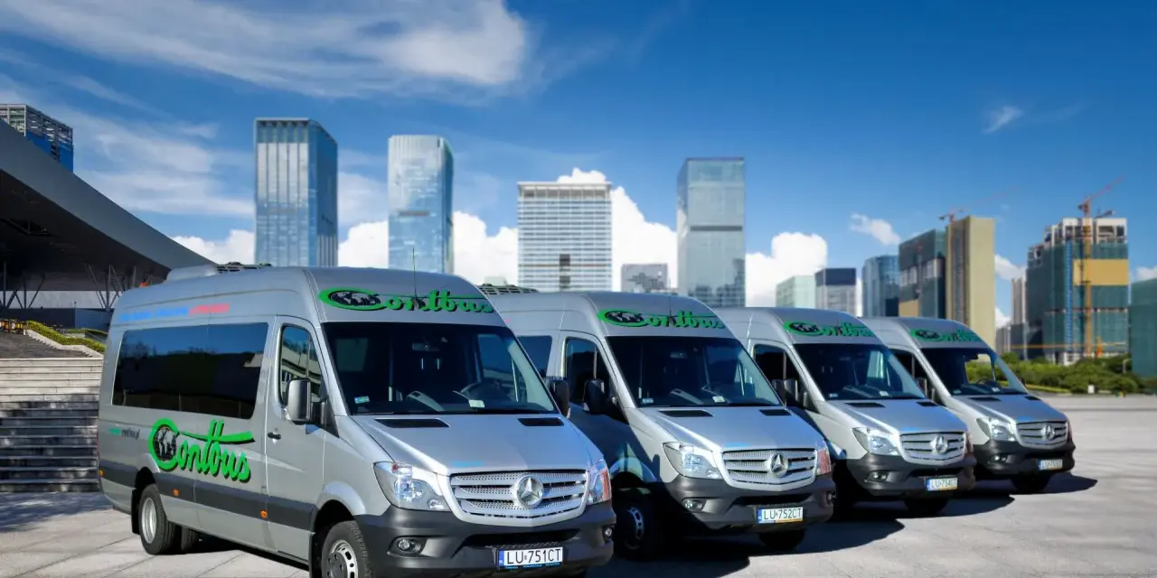 Rząd srebrnych busów Contbus na tle nowoczesnych wieżowców i błękitnego nieba.
