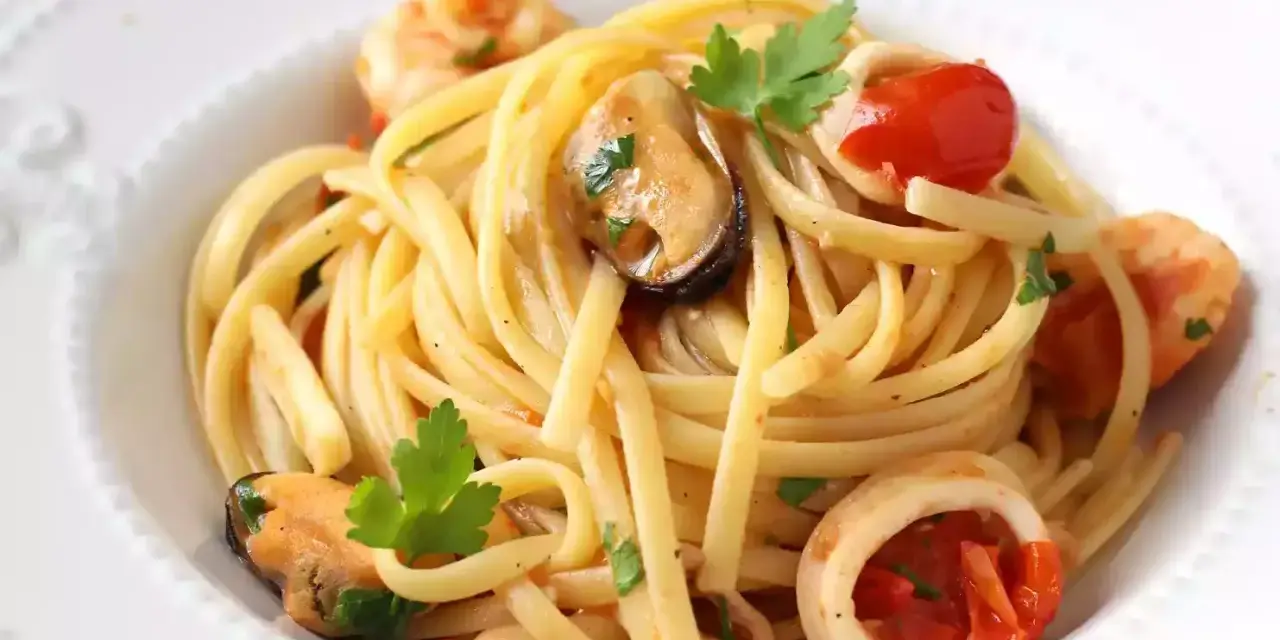 Tallarines con gambas al ajillo, mejillones y calamares, salpicados con perejil fresco y trocitos de tomate.