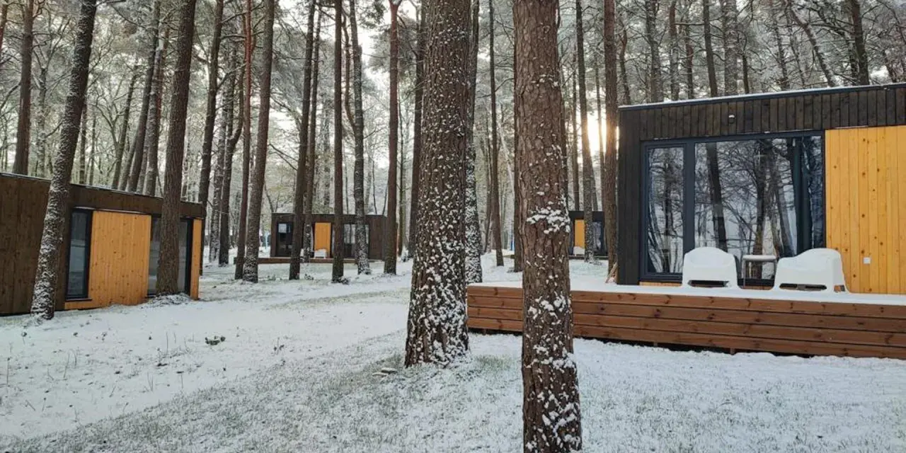 Nowoczesne domki nad morzem całoroczne w zimowej scenerii. Śnieg pokrywa trawę i drzewa, tworząc bajkowy krajobraz.