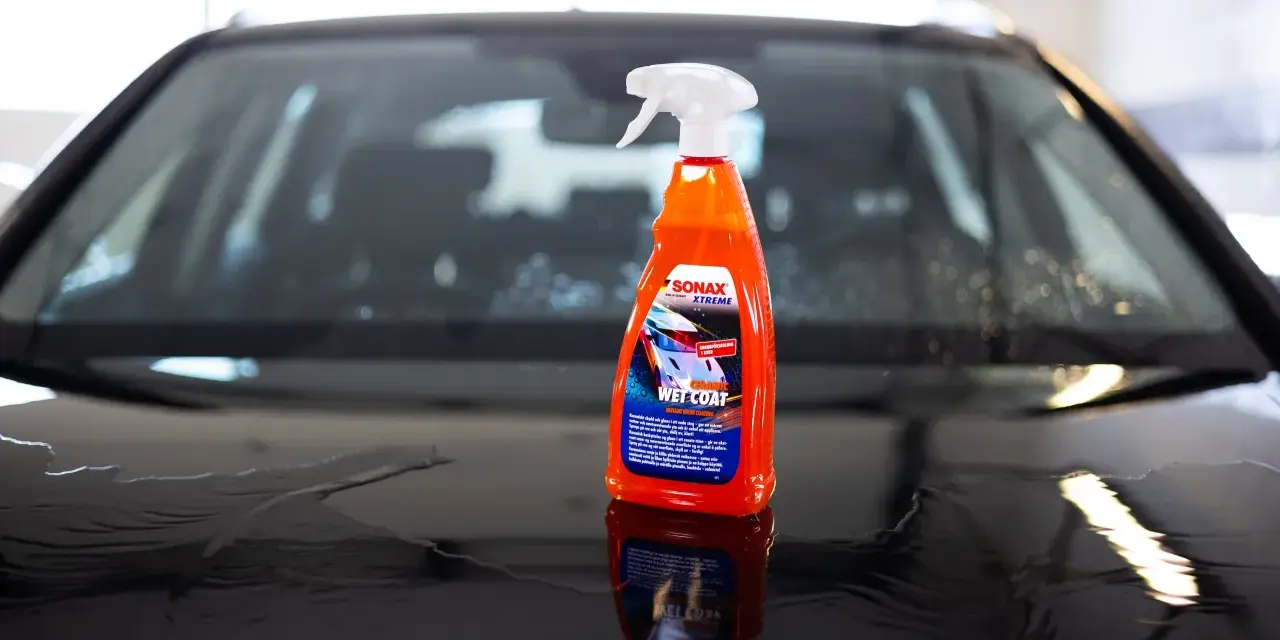 En flaska SONAX Xtreme Wet Coat står på en våt, mörk bilhuv.