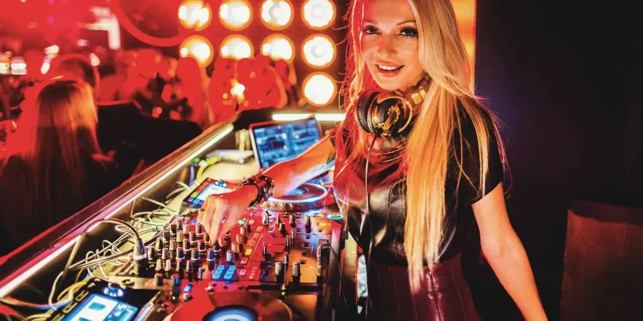 Une dj femme connue aux platines, mixant dans une ambiance club avec des lumières rouges.