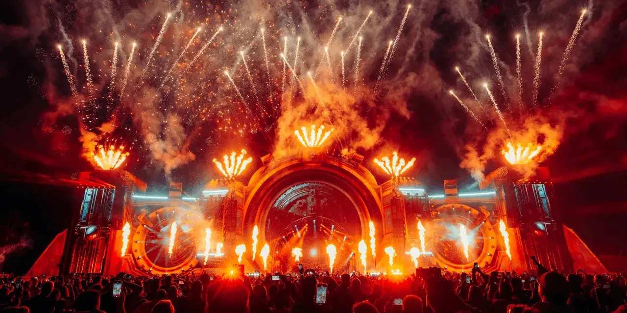 Spektakularny pokaz fajerwerków i płomieni na scenie podczas festiwalu Sunrise Festival 2026. Tłum ludzi z telefonami wzniesionymi ku górze.