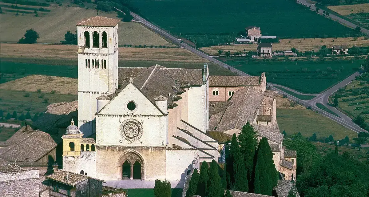 Basilica of Saint Francis of Assisi, a stunning example of Italian monasteries, with its iconic bell tower and rose window, nestled in a verdant landscape.