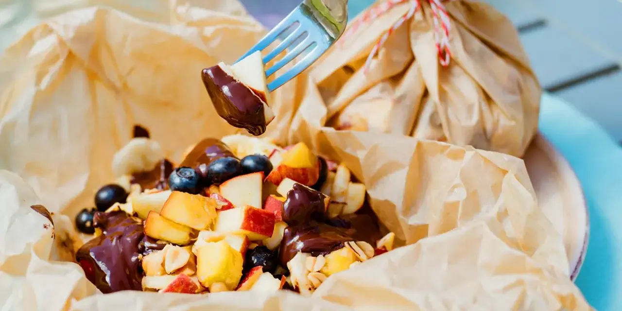 Fruchtiger Nachtisch vom Grill: Apfelstücke, Blaubeeren und Bananen mit Schokoladensauce, serviert in Papier.