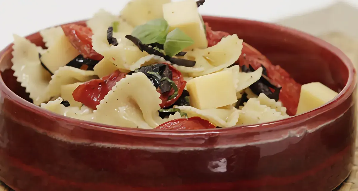 Deliciosa pasta farfalle con tomates secos, aceitunas negras, albahaca y cubos de queso. Una de las mejores recetas de pasta para disfrutar.