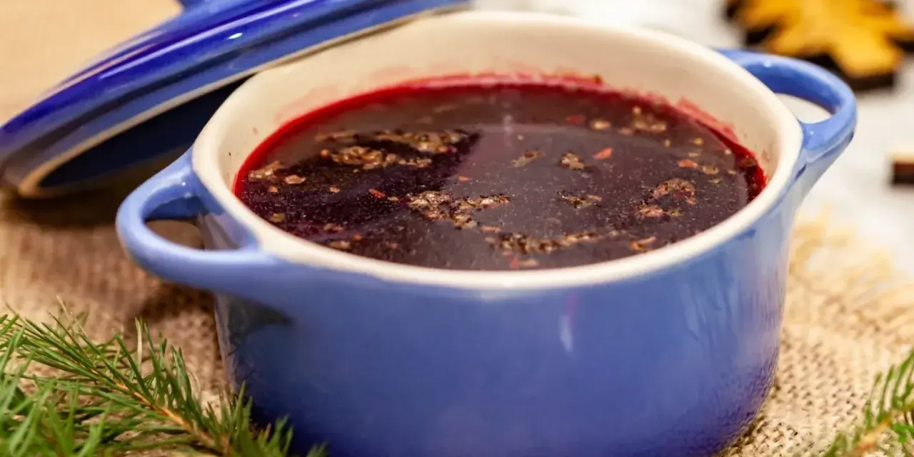 Aromaticzny barszcz czerwony wigilijny w niebieskiej wazie, ozdobionej gałązkami jodły i świątecznymi dekoracjami.