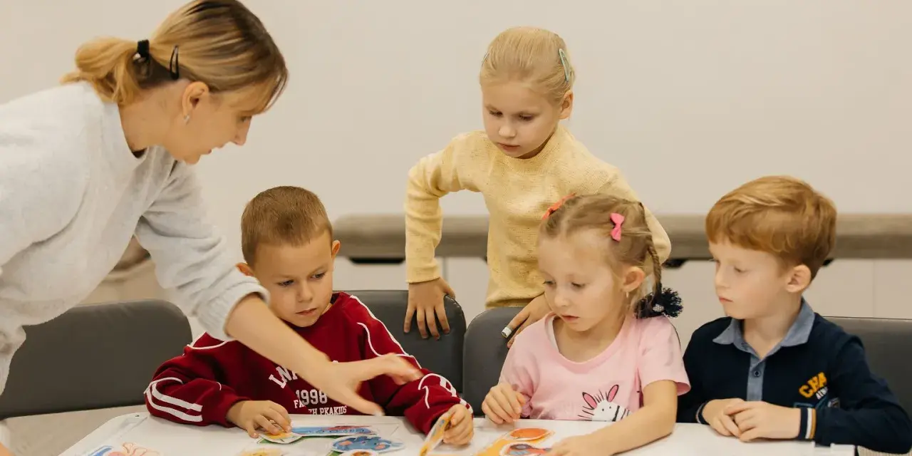 Nauczycielka pomaga dzieciom układać obrazki. Czy przedszkole może wypisać dziecko? Dzieci uczą się przez zabawę.