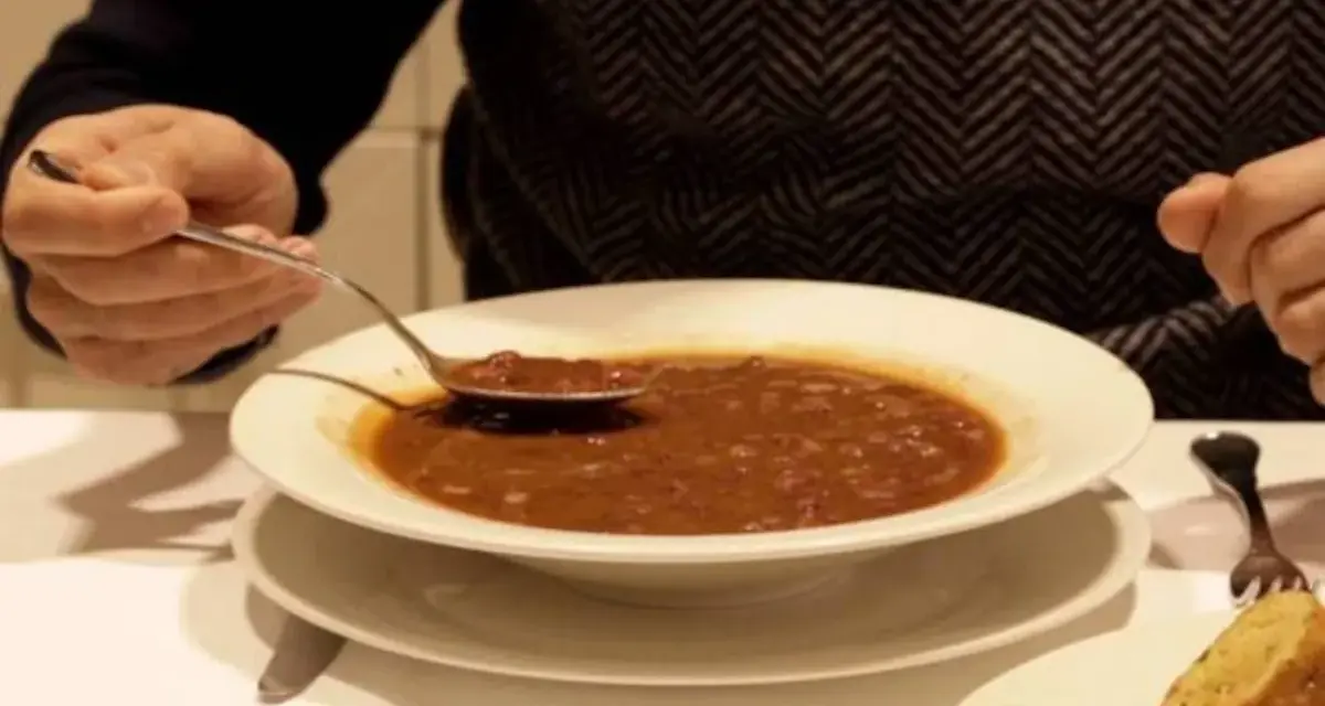 Persona prueba una cucharada de una humeante olla podrida, un plato reconfortante y tradicional.