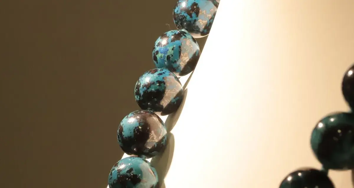 Collana di sfere in crisocolla pietra, con sfumature blu e nere, su sfondo chiaro e scuro.