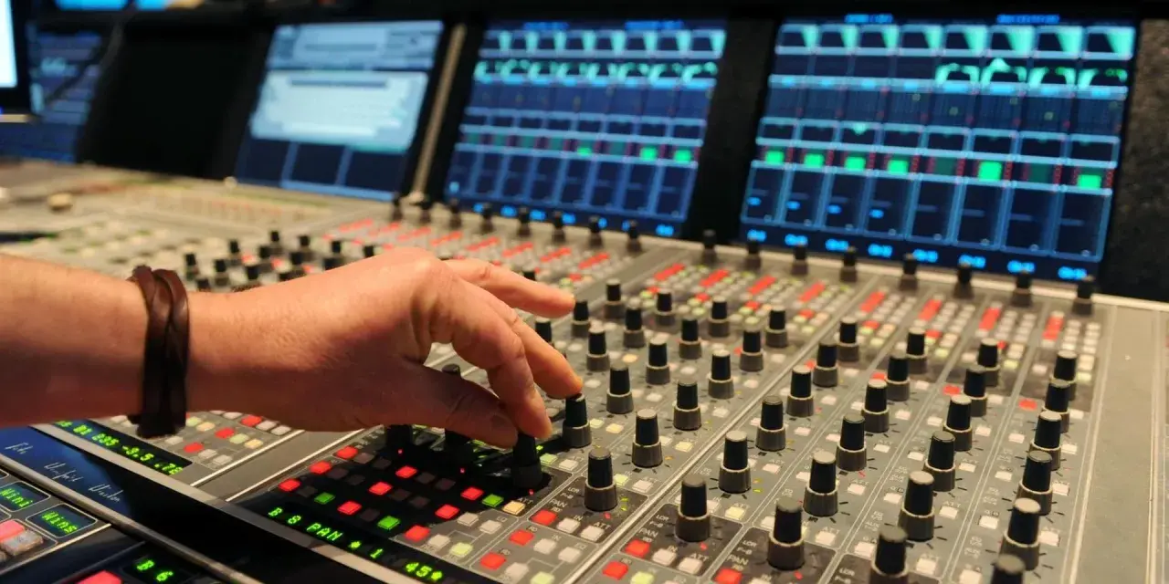 Hand am Mischpult, das an die Erfindung von Autotune erinnert. Tontechniker regelt Regler.