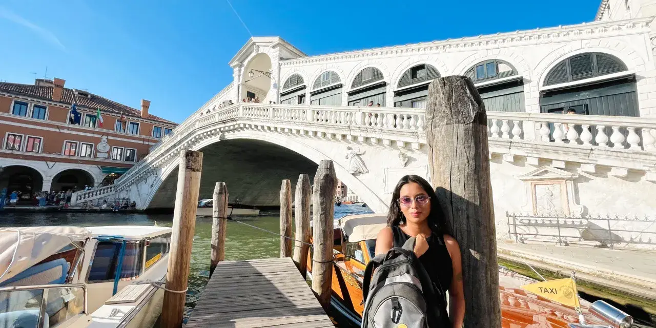 Una splendida giornata a Venezia, con la giovane donna che posa con il suo zaino davanti al Ponte di Rialto e ai taxi d'acqua.