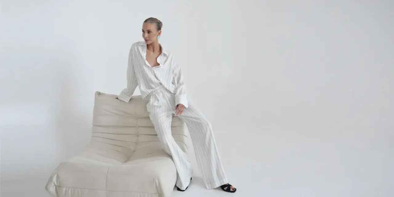 Elegancka kobieta w pasiastym komplecie, uosobienie quiet luxury, siedzi na kremowej sofie.
