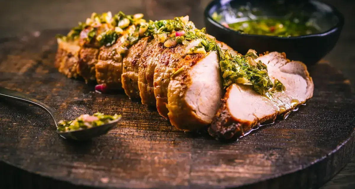 Jugoso solomillo de cerdo, cortado en rodajas y cubierto con una sabrosa salsa verde, servido en tabla de madera.