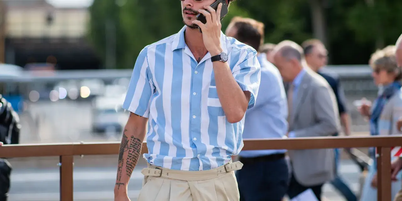 Hombre con camisa a rayas azules y blancas y tiro pantalón alto color beige, hablando por teléfono.