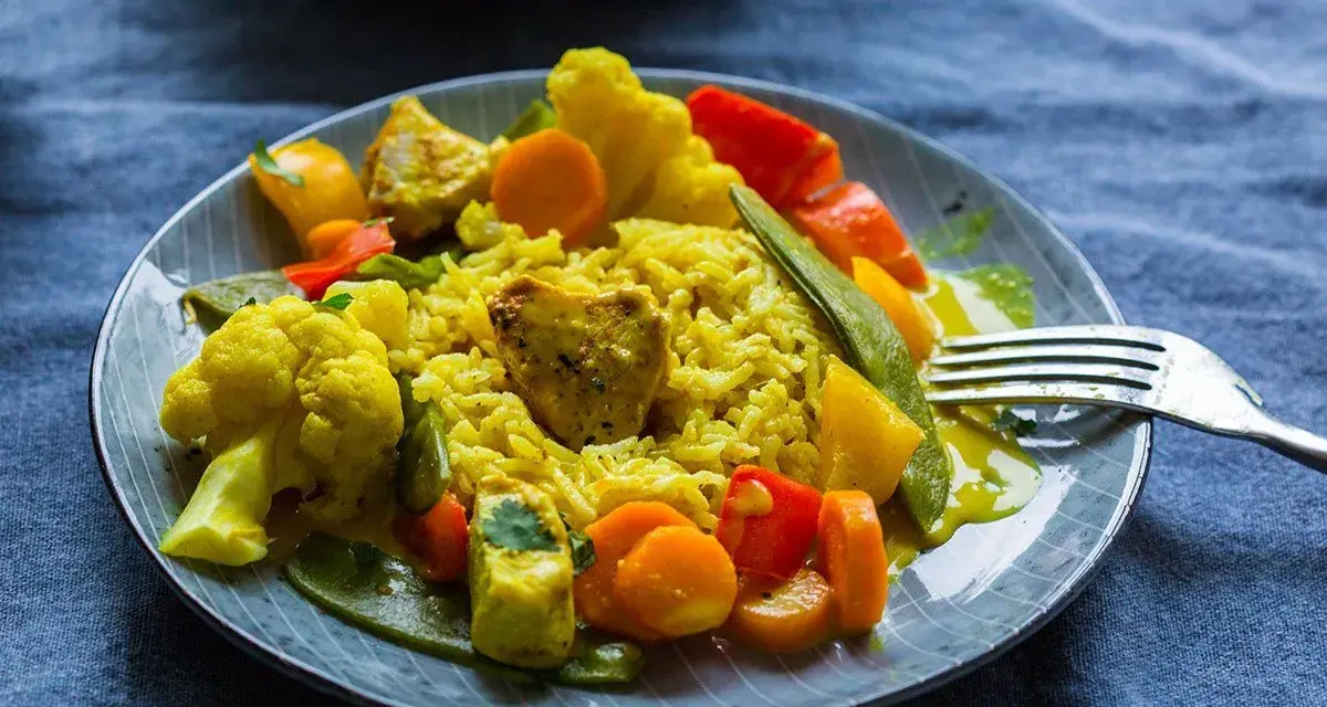 Ein Teller mit gelbem Reis, Blumenkohl, Karotten, Paprika und Erbsen. Ein köstliches Curry Geschnetzeltes, bereit zum Genießen.